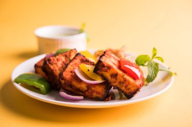 Paneer Tikka veya acı biber kebabı - Tandır Hint peyniri şişleri, beyaz tabakta servis edilir renkli kapsiyum, soğan ve yeşil sos ile