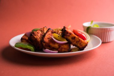 Paneer Tikka veya acı biber kebabı - Tandır Hint peyniri şişleri, beyaz tabakta servis edilir renkli kapsiyum, soğan ve yeşil sos ile