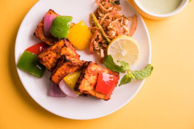 Paneer Tikka veya acı biber kebabı - Tandır Hint peyniri şişleri, beyaz tabakta servis edilir renkli kapsiyum, soğan ve yeşil sos ile