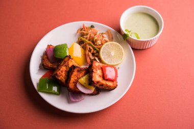 Paneer Tikka veya acı biber kebabı - Tandır Hint peyniri şişleri, beyaz tabakta servis edilir renkli kapsiyum, soğan ve yeşil sos ile