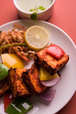 Paneer Tikka veya acı biber kebabı - Tandır Hint peyniri şişleri, beyaz tabakta servis edilir renkli kapsiyum, soğan ve yeşil sos ile
