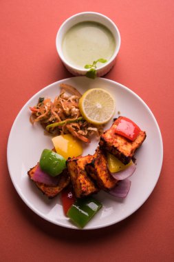 Paneer Tikka veya acı biber kebabı - Tandır Hint peyniri şişleri, beyaz tabakta servis edilir renkli kapsiyum, soğan ve yeşil sos ile
