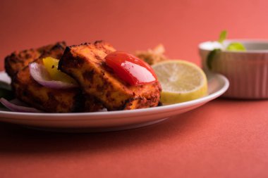 Paneer Tikka veya acı biber kebabı - Tandır Hint peyniri şişleri, beyaz tabakta servis edilir renkli kapsiyum, soğan ve yeşil sos ile