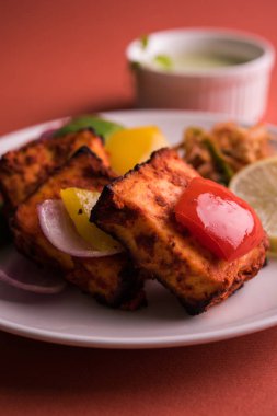 Paneer Tikka veya acı biber kebabı - Tandır Hint peyniri şişleri, beyaz tabakta servis edilir renkli kapsiyum, soğan ve yeşil sos ile