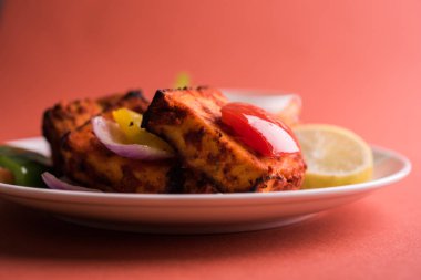 Paneer Tikka veya acı biber kebabı - Tandır Hint peyniri şişleri, beyaz tabakta servis edilir renkli kapsiyum, soğan ve yeşil sos ile