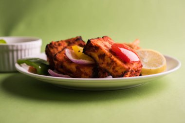 Paneer Tikka veya acı biber kebabı - Tandır Hint peyniri şişleri, beyaz tabakta servis edilir renkli kapsiyum, soğan ve yeşil sos ile
