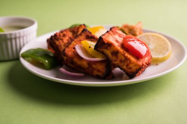 Paneer Tikka veya acı biber kebabı - Tandır Hint peyniri şişleri, beyaz tabakta servis edilir renkli kapsiyum, soğan ve yeşil sos ile