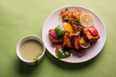 Paneer Tikka veya acı biber kebabı - Tandır Hint peyniri şişleri, beyaz tabakta servis edilir renkli kapsiyum, soğan ve yeşil sos ile