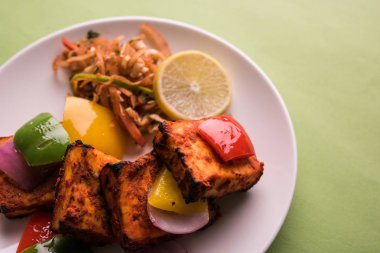 Paneer Tikka veya acı biber kebabı - Tandır Hint peyniri şişleri, beyaz tabakta servis edilir renkli kapsiyum, soğan ve yeşil sos ile