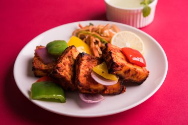 Paneer Tikka veya acı biber kebabı - Tandır Hint peyniri şişleri, beyaz tabakta servis edilir renkli kapsiyum, soğan ve yeşil sos ile