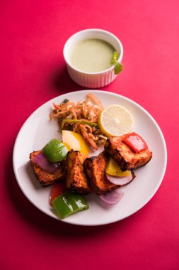 Paneer Tikka veya acı biber kebabı - Tandır Hint peyniri şişleri, beyaz tabakta servis edilir renkli kapsiyum, soğan ve yeşil sos ile