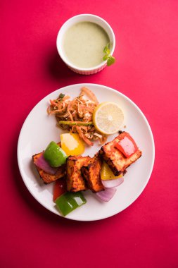 Paneer Tikka veya acı biber kebabı - Tandır Hint peyniri şişleri, beyaz tabakta servis edilir renkli kapsiyum, soğan ve yeşil sos ile