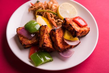 Paneer Tikka veya acı biber kebabı - Tandır Hint peyniri şişleri, beyaz tabakta servis edilir renkli kapsiyum, soğan ve yeşil sos ile