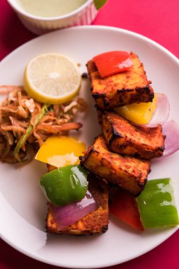 Paneer Tikka veya acı biber kebabı - Tandır Hint peyniri şişleri, beyaz tabakta servis edilir renkli kapsiyum, soğan ve yeşil sos ile