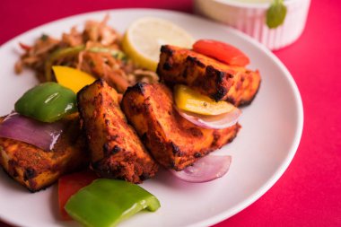 Paneer Tikka veya acı biber kebabı - Tandır Hint peyniri şişleri, beyaz tabakta servis edilir renkli kapsiyum, soğan ve yeşil sos ile