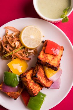 Paneer Tikka veya acı biber kebabı - Tandır Hint peyniri şişleri, beyaz tabakta servis edilir renkli kapsiyum, soğan ve yeşil sos ile