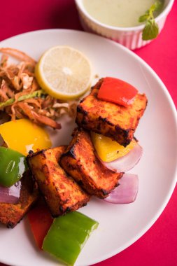 Paneer Tikka veya acı biber kebabı - Tandır Hint peyniri şişleri, beyaz tabakta servis edilir renkli kapsiyum, soğan ve yeşil sos ile