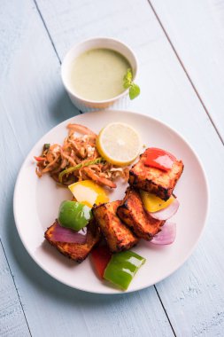 Paneer Tikka veya acı biber kebabı - Tandır Hint peyniri şişleri, beyaz tabakta servis edilir renkli kapsiyum, soğan ve yeşil sos ile