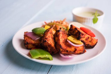 Paneer Tikka veya acı biber kebabı - Tandır Hint peyniri şişleri, beyaz tabakta servis edilir renkli kapsiyum, soğan ve yeşil sos ile