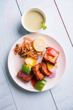 Paneer Tikka veya acı biber kebabı - Tandır Hint peyniri şişleri, beyaz tabakta servis edilir renkli kapsiyum, soğan ve yeşil sos ile