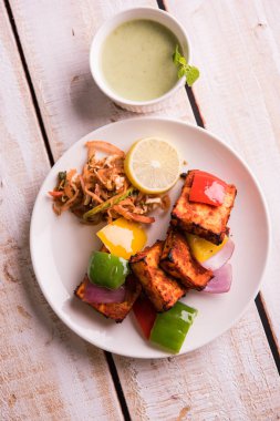 Paneer Tikka veya acı biber kebabı - Tandır Hint peyniri şişleri, beyaz tabakta servis edilir renkli kapsiyum, soğan ve yeşil sos ile