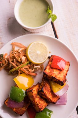 Paneer Tikka veya acı biber kebabı - Tandır Hint peyniri şişleri, beyaz tabakta servis edilir renkli kapsiyum, soğan ve yeşil sos ile