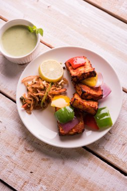 Paneer Tikka veya acı biber kebabı - Tandır Hint peyniri şişleri, beyaz tabakta servis edilir renkli kapsiyum, soğan ve yeşil sos ile