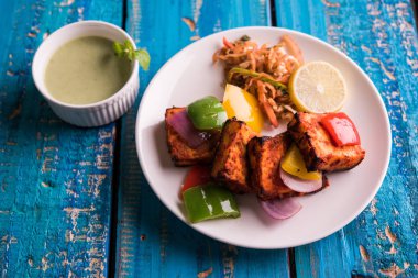Paneer Tikka veya acı biber kebabı - Tandır Hint peyniri şişleri, beyaz tabakta servis edilir renkli kapsiyum, soğan ve yeşil sos ile