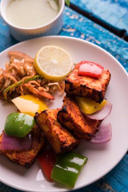 Paneer Tikka veya acı biber kebabı - Tandır Hint peyniri şişleri, beyaz tabakta servis edilir renkli kapsiyum, soğan ve yeşil sos ile