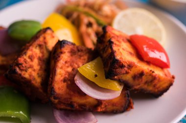 Paneer Tikka veya acı biber kebabı - Tandır Hint peyniri şişleri, beyaz tabakta servis edilir renkli kapsiyum, soğan ve yeşil sos ile