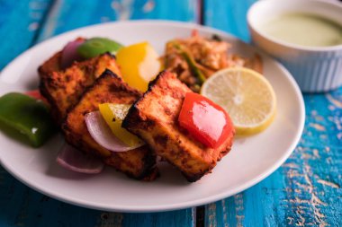 Paneer Tikka veya acı biber kebabı - Tandır Hint peyniri şişleri, beyaz tabakta servis edilir renkli kapsiyum, soğan ve yeşil sos ile