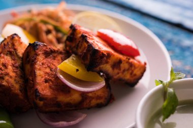Paneer Tikka veya acı biber kebabı - Tandır Hint peyniri şişleri, beyaz tabakta servis edilir renkli kapsiyum, soğan ve yeşil sos ile