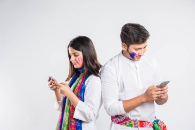 Holi Festivali 'nde akıllı telefonla meşgul Hintli bir çift. Yüzleri renklerle boyanmış, beyaz arka planda izole edilmiş.