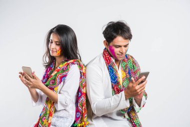Holi Festivali 'nde martphone kullanan Hintli çift. Yüzleri renklerle boyanmış, beyaz arka planda izole edilmiş.