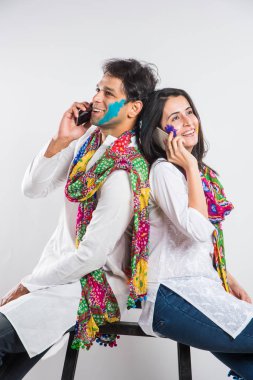 Holi Festivali 'nde martphone kullanan Hintli çift. Yüzleri renklerle boyanmış, beyaz arka planda izole edilmiş.