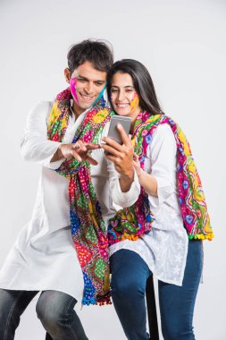 Holi Festivali 'nde martphone kullanan Hintli çift. Yüzleri renklerle boyanmış, beyaz arka planda izole edilmiş.