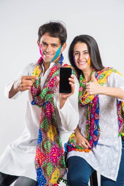 Holi Festivali 'nde martphone kullanan Hintli çift. Yüzleri renklerle boyanmış, beyaz arka planda izole edilmiş.