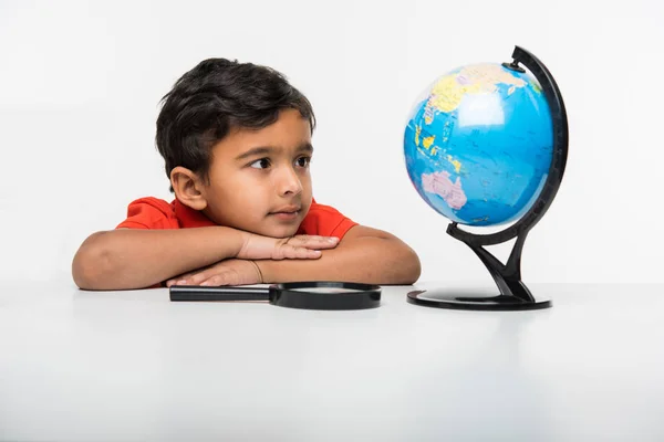 Niño indio observando o estudiando el modelo de globo educativo con lupa — Foto de Stock