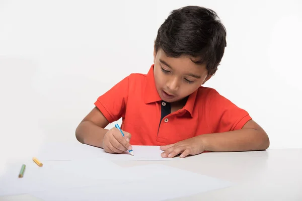 Индийский мальчик ребенок с цветным карандашом для рисования, сидя за белым столом — стоковое фото