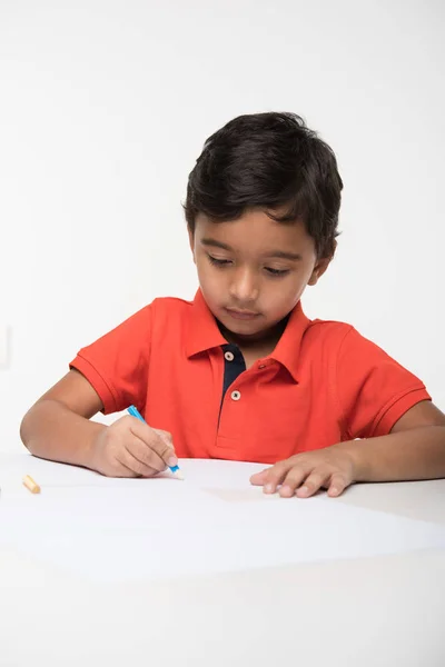 Індійська хлопчика дитини за допомогою барвисті олівець для малювання, сидячи за столом білий — стокове фото