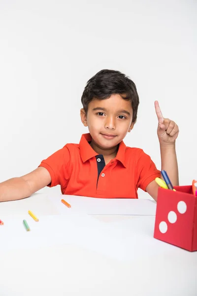 Indiana menino criança usando lápis colorido para desenho, sentado na mesa branca — Fotografia de Stock