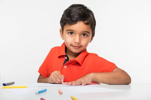 Enfant garçon indien utilisant crayon coloré pour le dessin, assis à la table blanche — Photo