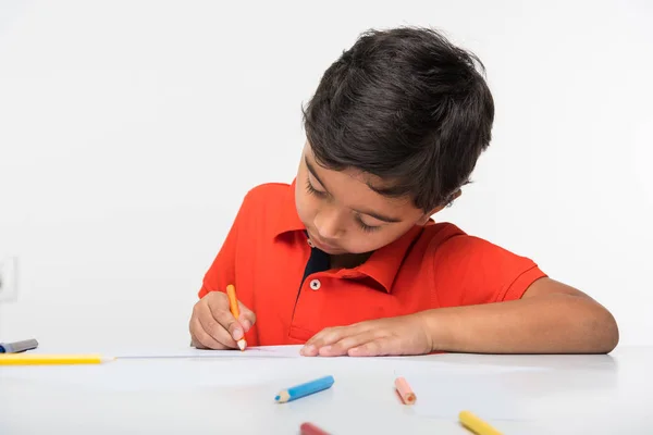 Ινδική αγόρι παιδί χρησιμοποιώντας πολύχρωμα μολύβι για την κατάρτιση, κάθεται στο τραπέζι λευκό — Φωτογραφία Αρχείου