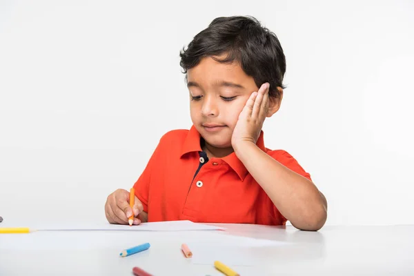 Indiana menino criança usando lápis colorido para desenho, sentado na mesa branca — Fotografia de Stock