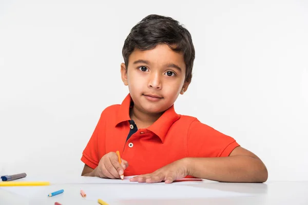 Indian boy child using colourful pencil for drawing, sitting at white table — Stock Photo, Image