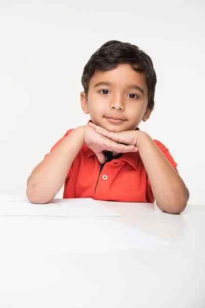 Mutlu Hint çingene çocuk çocuk okul masada oturan izole beyaz zemin üzerine Hint çocuk masada çene ile her iki elleri üzerinde oturuyor. — Stok fotoğraf