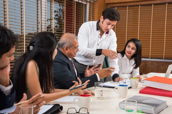 Combinando su experiencia. Joven y guapo empresario y mujer india haciendo gestos y discutiendo algo con sus compañeros de trabajo mientras están sentados en la mesa de la oficina, enfoque selectivo — Foto de Stock