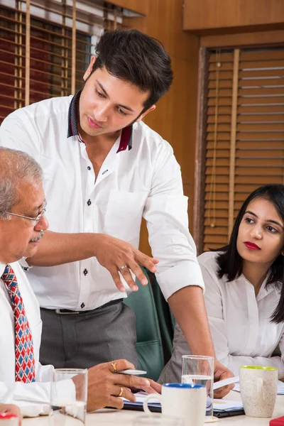 Combinando su experiencia. Joven y guapo empresario y mujer india haciendo gestos y discutiendo algo con sus compañeros de trabajo mientras están sentados en la mesa de la oficina, enfoque selectivo — Foto de Stock