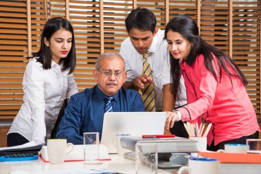 Yeni plan memnun. Gençlerin Grup 4-5 Hint neşeli ve gülümseme yaslanmış ofiste tabloda için süre ile laptop arıyorum bir deneyimli iş adamı