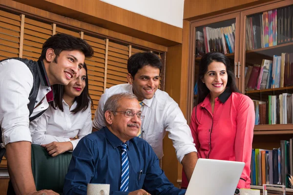 Satisfied with new plan. Group of four to five Indian cheerful young people and one experienced businessman looking at laptop with smile while leaning to the table in office — Stock Photo, Image